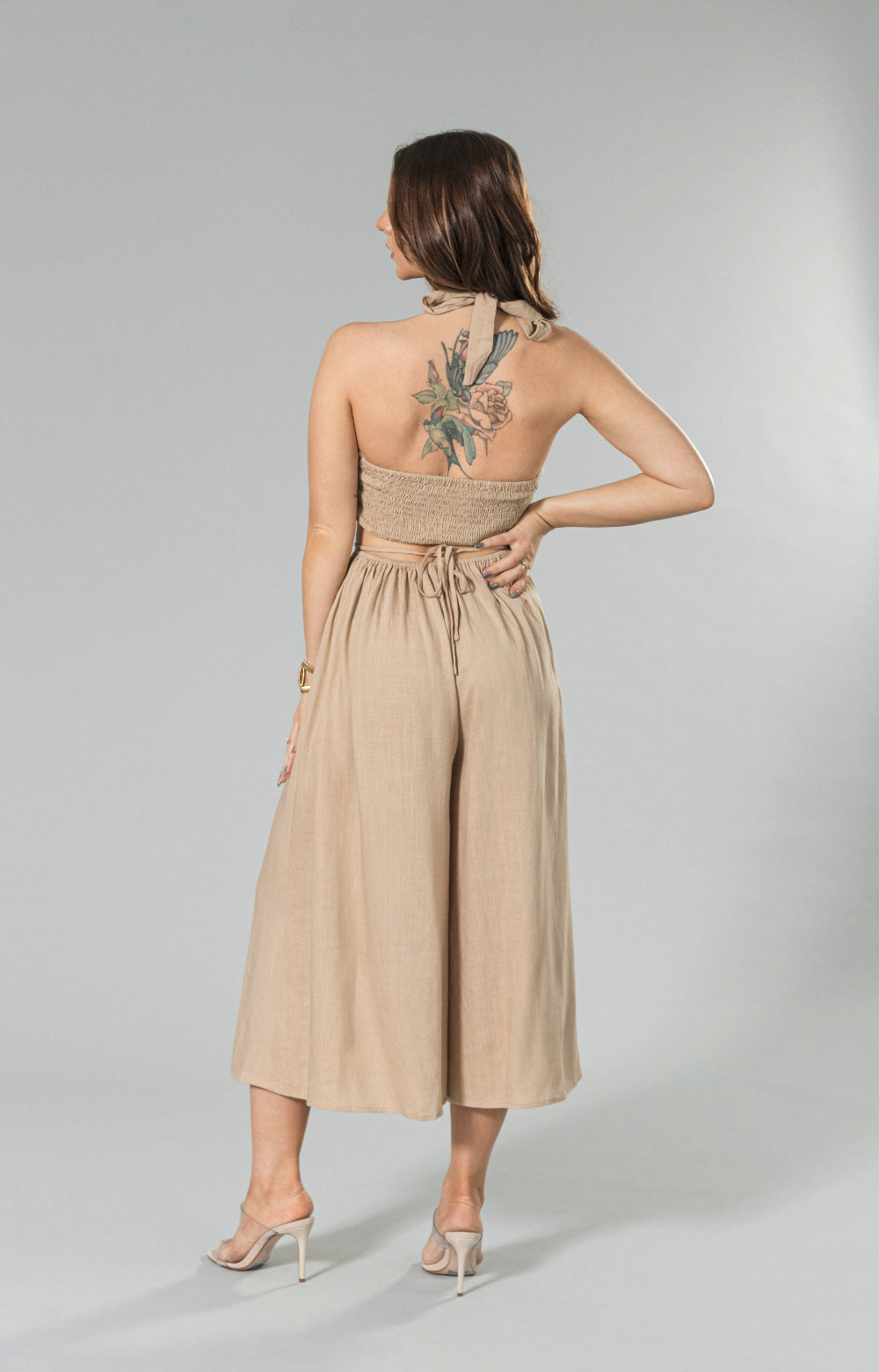 Get ready to turn heads in our stylish Sahara linen wide leg jumpsuit. Made from lightweight and breathable linen blend fabric, this halter neck jumpsuit features a wide leg capri design, back smocking for a comfortable fit, and a waist tie to enhance your figure. The halter cut out detail adds a playful touch, making it the perfect choice for any occasion. 

